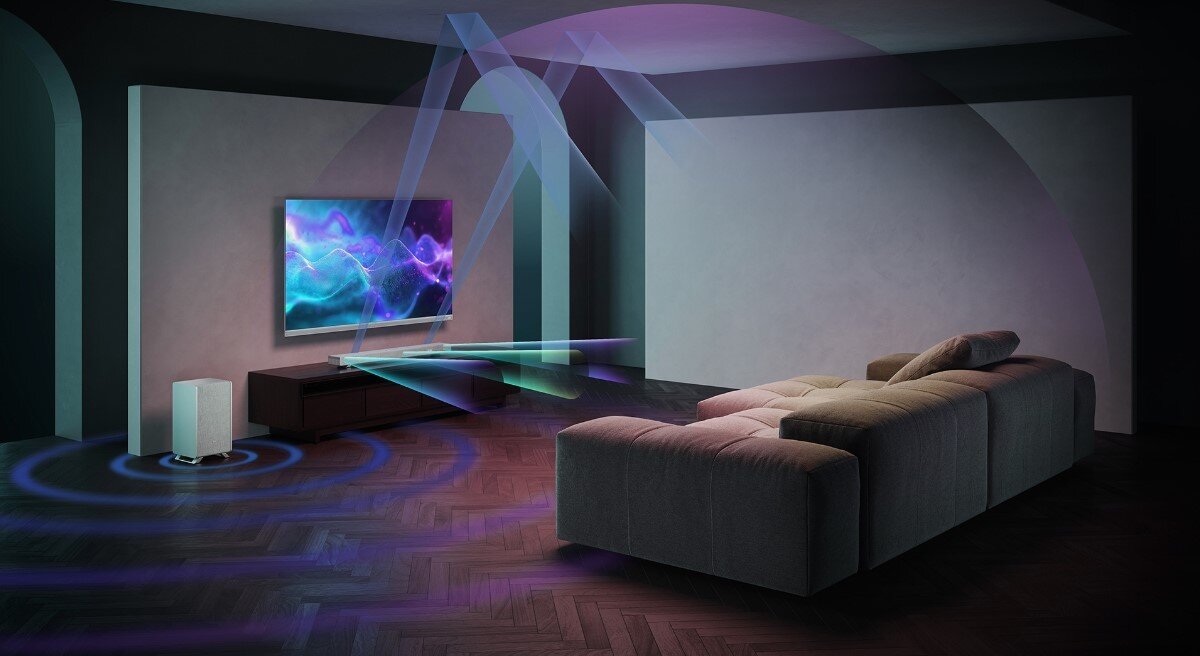 W salonie znajduje się telewizor na ścianie, przed którym stoi soundbar i bezprzewodowy subwoofer. Na ekranie telewizora widoczne są kolorowe fale, a wokół soundbara i subwoofera przedstawione są efekty dźwiękowe w postaci kolorowych linii.