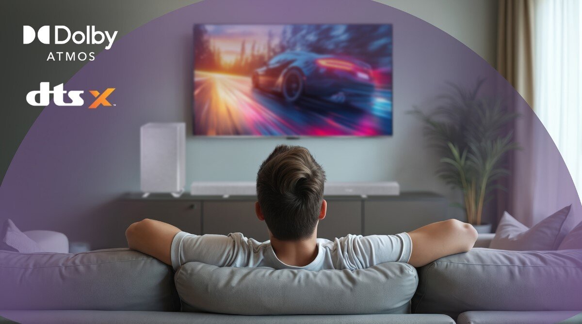 Osoba siedzi na kanapie przed telewizorem, na którym wyświetlany jest dynamiczny obraz samochodu. W lewym górnym rogu widoczne są loga \'Dolby Atmos\' i \'dts X\'.