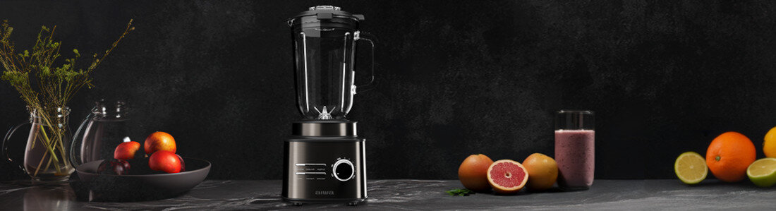 Na ciemnym tle znajduje się blender kielichowy z przezroczystym pojemnikiem i czarną podstawą. Obok widoczne są owoce, w tym pomarańcze, limonki i szklanka z różowym napojem.