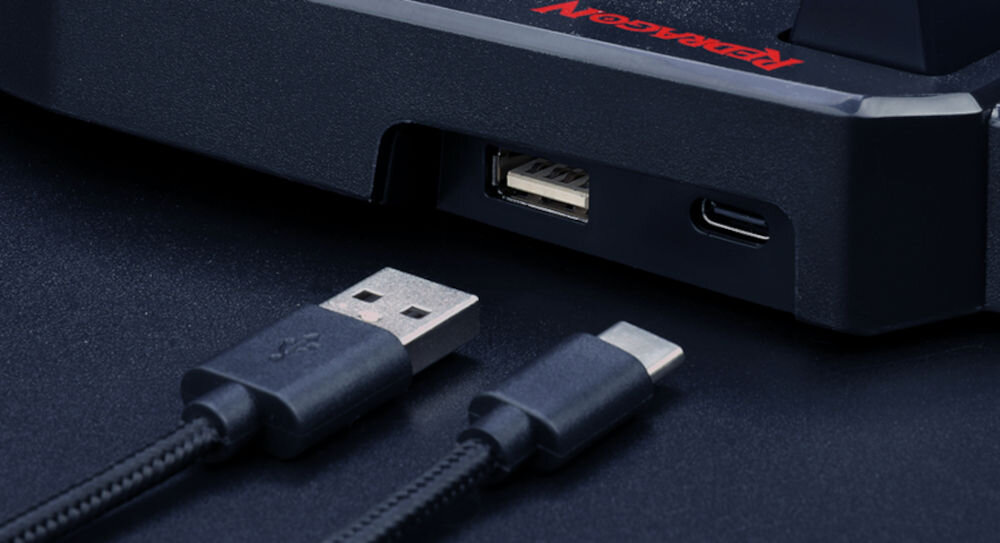 Na obrazie widoczny jest fragment urządzenia z dwoma portami: USB i USB-C. Obok znajdują się dwa kable z końcówkami pasującymi do tych portów, a na urządzeniu widnieje logo \'Redragon\'.