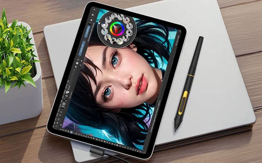 Tablet graficzny BOSTO BT-101C Tablet graficzny leżący ukośnie na zamkniętym laptopie obok rysika, w tle widoczna część doniczki z zieloną rośliną, rysik, poziomy nacisku, działanie