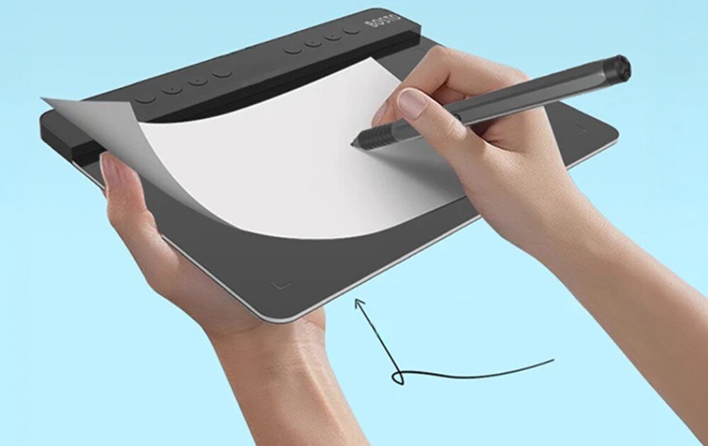 Tablet graficzny BOSTO T1060K Dłonie trzymające tablet, na którym leży zagięty arkusz białego papieru, po którym rysuje bezprzewodowe pióro, symbolizując strukturę podłoża, wymiary, przeznaczenie, wielkość