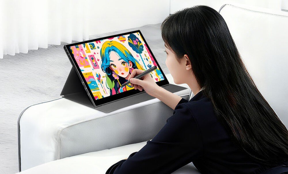 Osoba używa tabletu graficznego z rysikiem, na ekranie widoczna jest kolorowa ilustracja postaci z niebieskimi włosami. Tablet jest ustawiony na białej kanapie, a w tle widać białe zasłony.