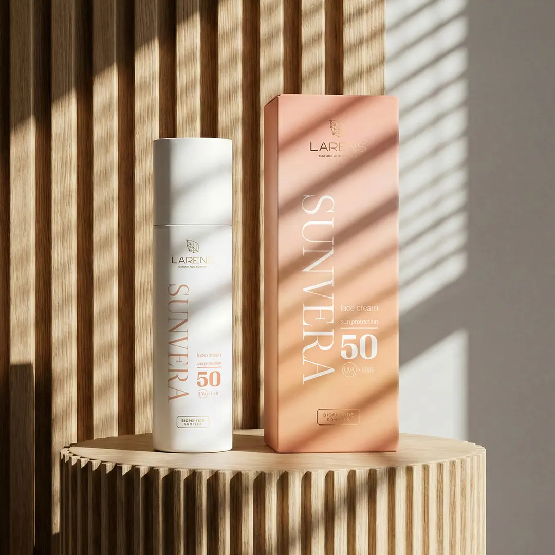 Na drewnianym tle znajduje się biały flakon i pomarańczowe pudełko z napisem \'LARENS SUNVERA face cream sun protection 50 UVA + UVB\'.