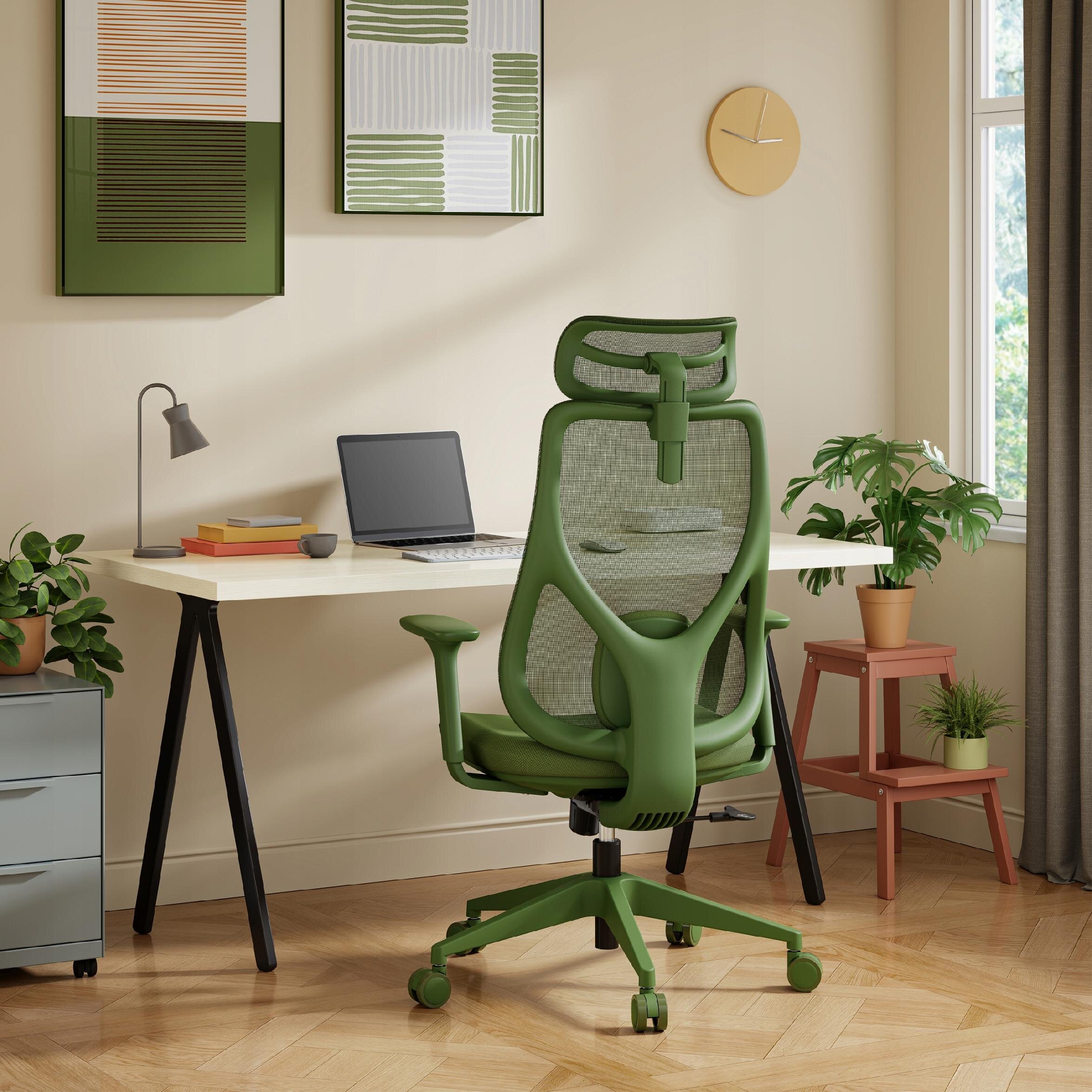 Zielony fotel biurowy o ergonomicznym kształcie stoi przy biurku z laptopem i lampką. W tle znajdują się rośliny doniczkowe oraz dwa obrazy na ścianie.