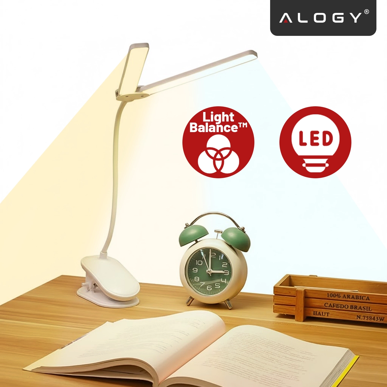 Na drewnianym biurku znajduje się lampka biurkowa z klipsem, otwarta książka, zielony budzik oraz drewniane pudełko. W tle widoczne są dwa czerwone symbole z napisami \'Light Balance™\' i \'LED\', a w górnym rogu logo \'ALOGY\'.