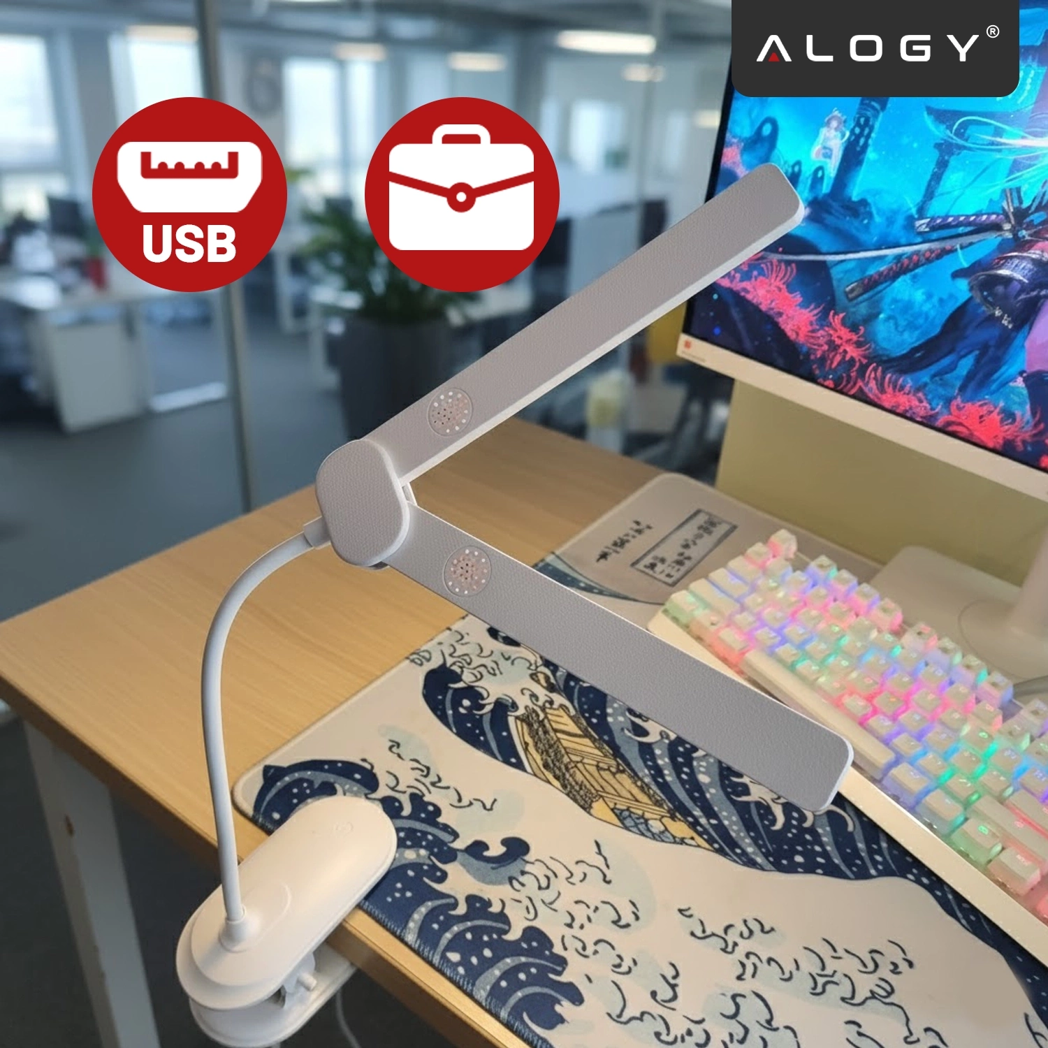 Na biurku znajduje się biała lampka biurkowa z klipsem, obok kolorowej klawiatury i monitora. W tle widoczne są dwa czerwone symbole: USB i teczka, a w prawym górnym rogu logo \'ALOGY\'.