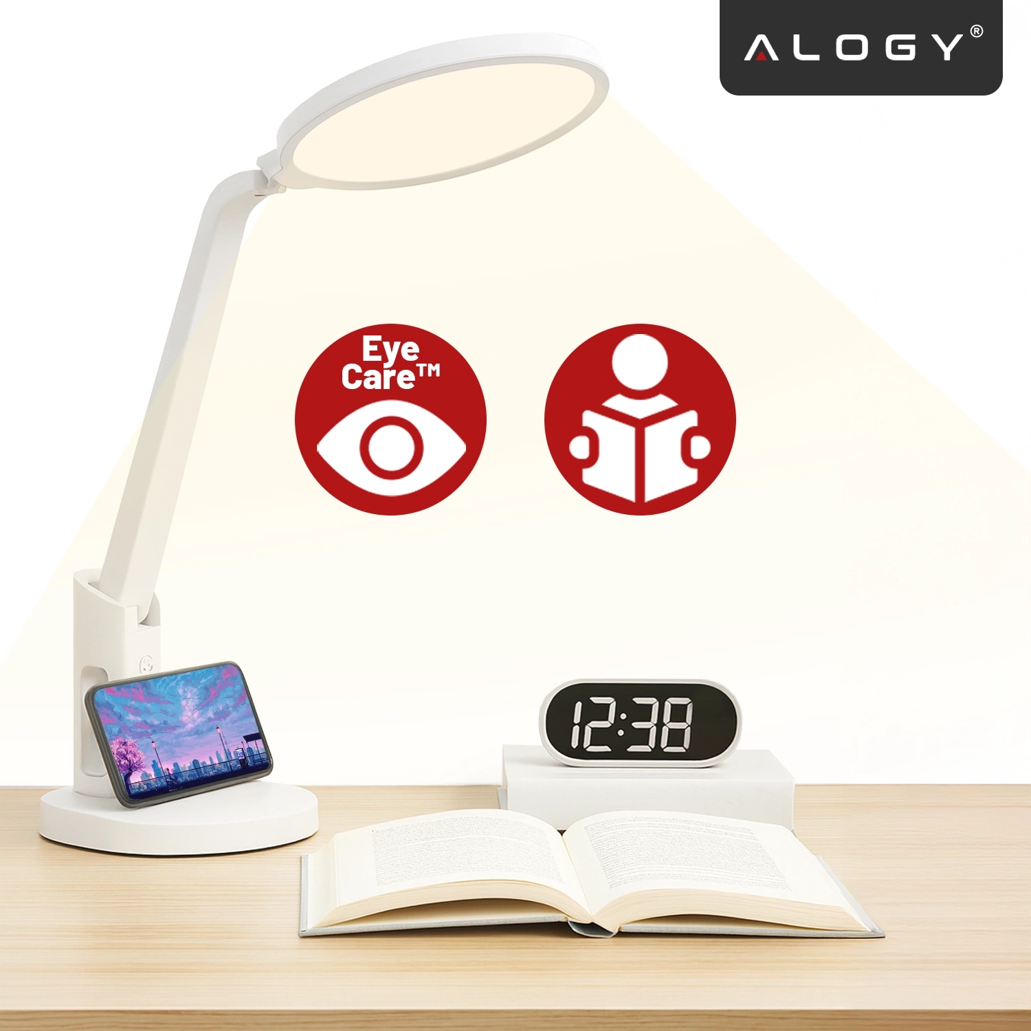 Na biurku znajduje się lampka biurkowa z regulowanym ramieniem, obok której stoi otwarta książka i zegar elektroniczny pokazujący godzinę 12:38. Na ścianie widoczne są dwa czerwone symbole: oko z napisem \'Eye Care™\' oraz postać z książką, a w rogu logo \'ALOGY\'.