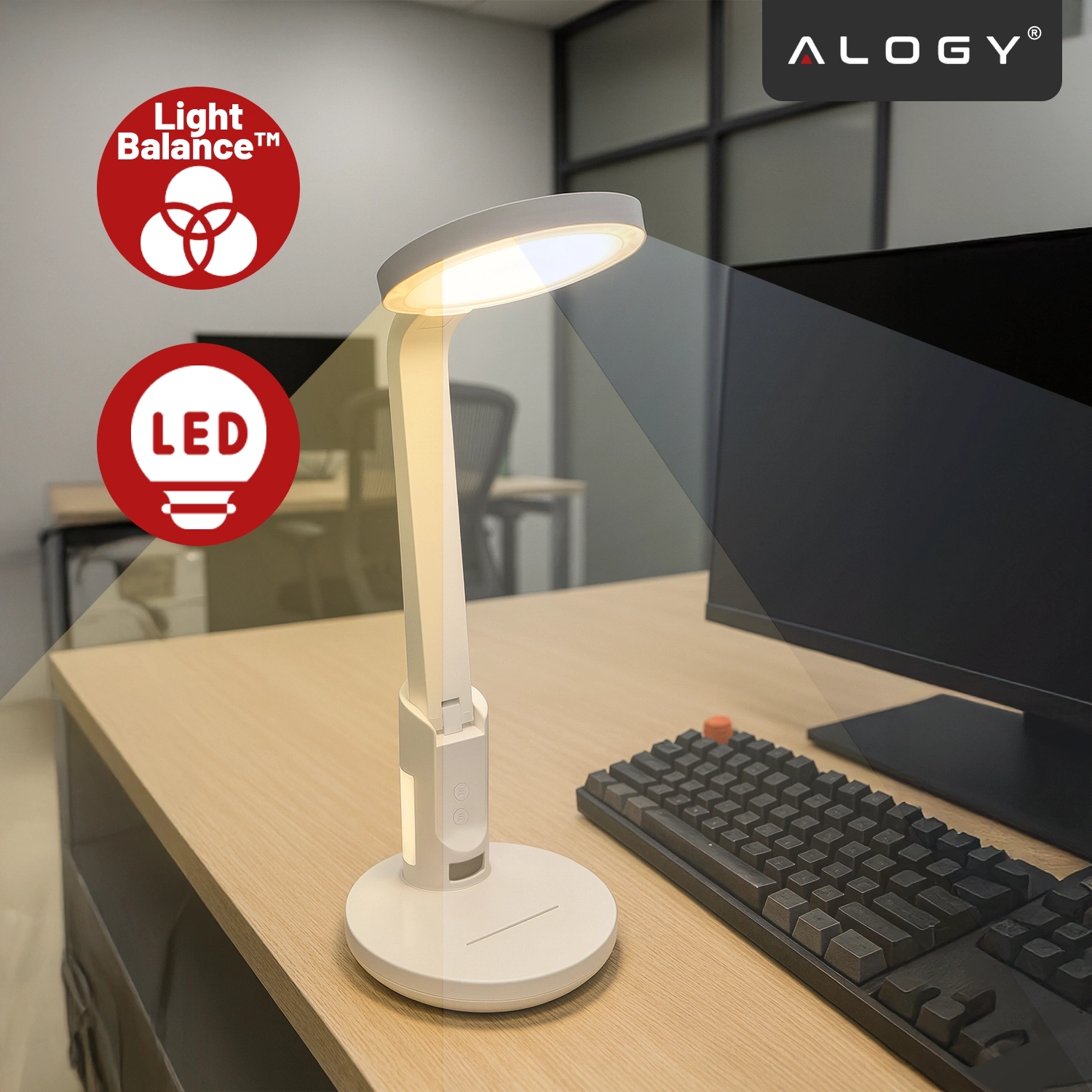 Na biurku znajduje się biała lampka biurkowa LED z regulowanym światłem, obok klawiatury i monitora. W lewym górnym rogu widoczne są czerwone ikony z napisami \'Light Balance™\' i \'LED\', a w prawym górnym rogu logo \'ALOGY\'.