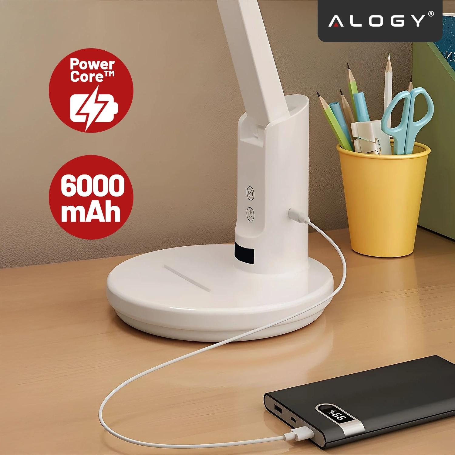 Na biurku znajduje się biała lampka biurkowa z regulowanym światłem, podłączona do powerbanku. Obok lampki stoi żółty kubek z przyborami do pisania, a na obrazie widoczne są napisy \'Power Core™\' i \'6000 mAh\'.