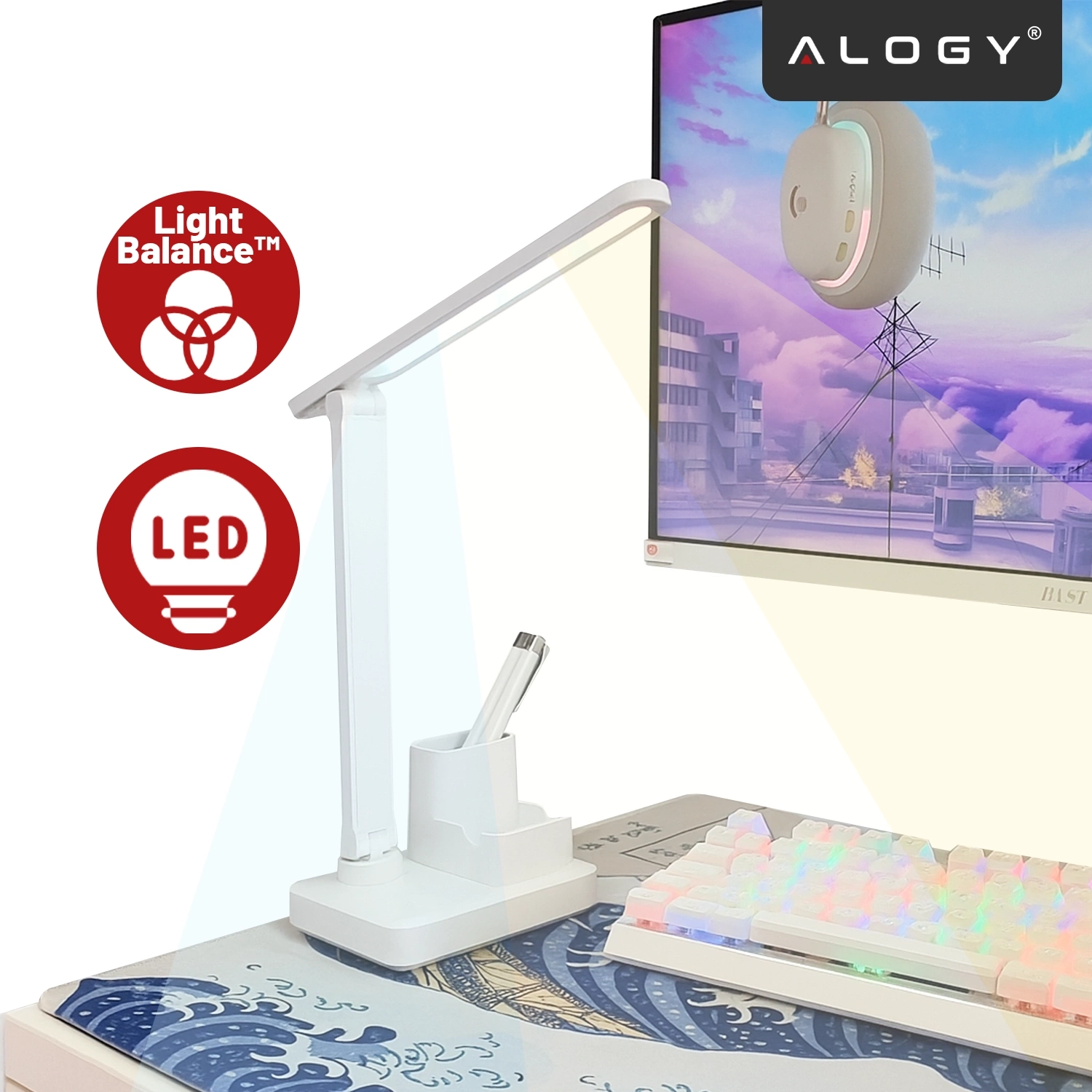 Na biurku znajduje się biała lampka biurkowa LED z organizerem na długopisy. Obok lampki widoczne są dwa czerwone symbole z napisami \'Light Balance™\' i \'LED\', a w tle ekran monitora z grafiką i logo \'ALOGY\'.