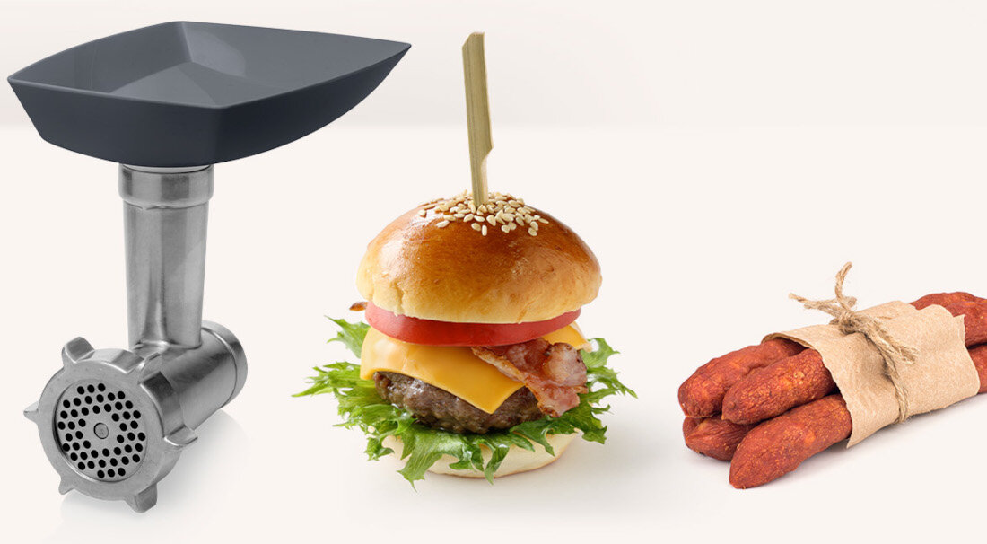 Obraz przedstawia metalową maszynkę do mięsa, burgera z bułką, serem, bekonem, pomidorem i sałatą oraz wiązkę kiełbas zawiązanych sznurkiem.