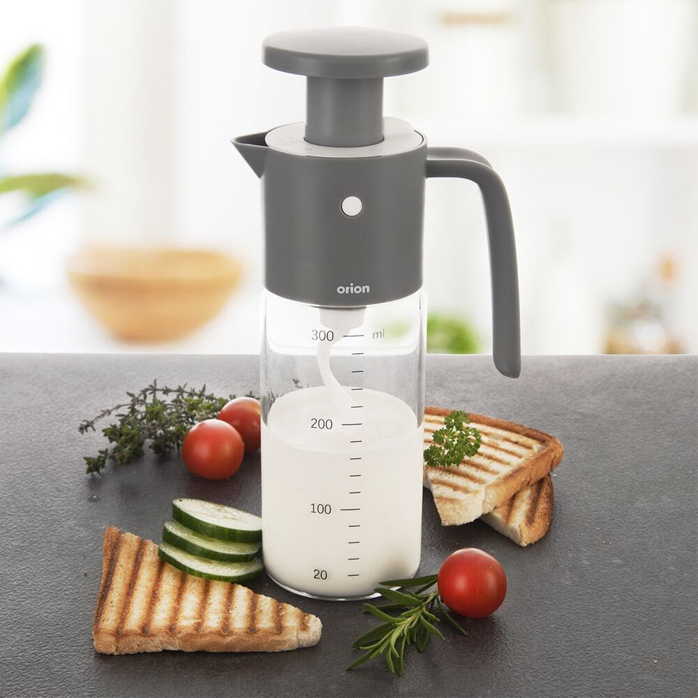 Na obrazie widoczna jest przezroczysta butelka z miarką do 300 ml, z szarym uchwytem i pokrywką, oznaczona napisem \'orion\'. Wokół butelki znajdują się plasterki ogórka, pomidorki koktajlowe, zioła i kawałki tostów.