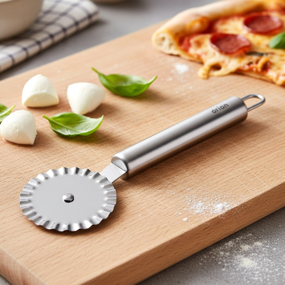 Na drewnianej desce do krojenia leży stalowe radełko do ciasta z ząbkowanym kółkiem. Obok znajdują się kawałki mozzarelli, liście bazylii i kawałek pizzy.