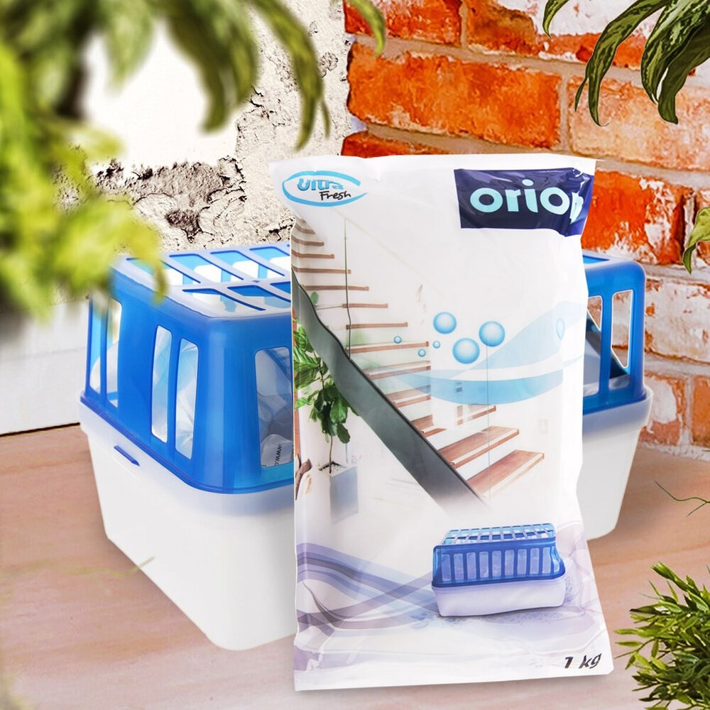 Na obrazie widoczny jest biały worek z napisem \'Ultra Fresh\' i \'orion\', przedstawiający schody i niebieskie bąbelki. Obok znajduje się biało-niebieski pojemnik z kratką, a w tle ceglana ściana i rośliny.