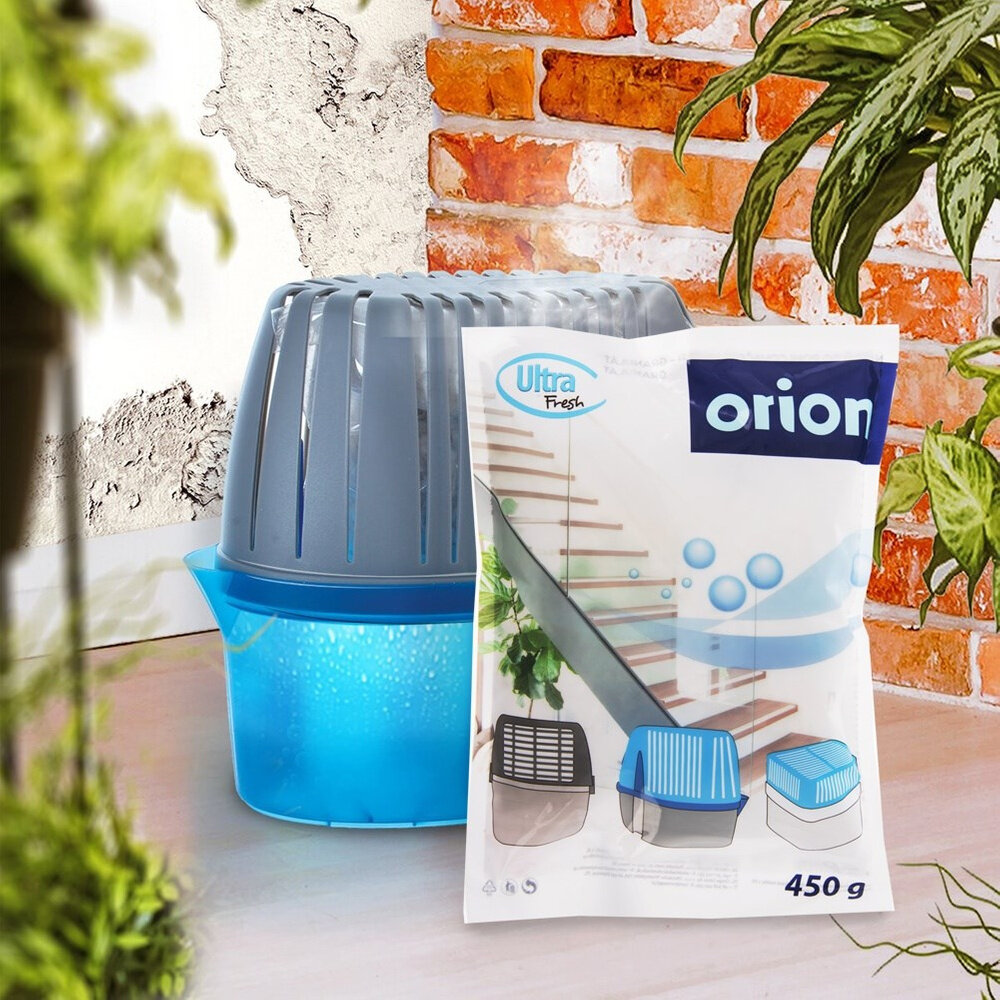 Na obrazie widoczny jest pochłaniacz wilgoci z niebieskim pojemnikiem oraz opakowanie granulatu Ultra Fresh 450 g z logo \'orion\'. W tle znajduje się ściana z cegieł i rośliny.