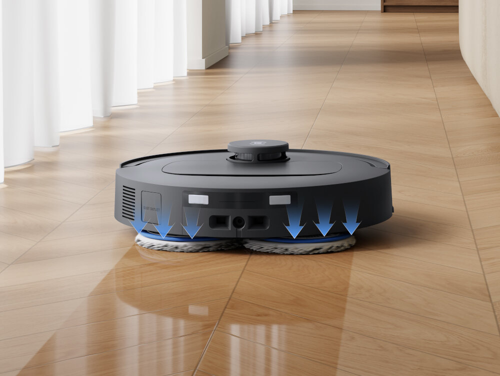 Robot sprzątający na drewnianej podłodze z widocznymi niebieskimi strzałkami wskazującymi na jego funkcję czyszczenia. W tle znajdują się białe zasłony i ściana.