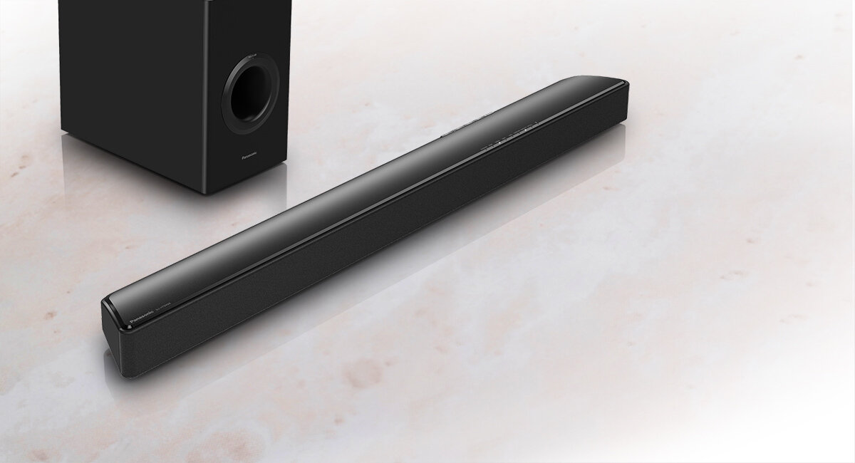 Na obrazie widoczny jest czarny soundbar oraz subwoofer na jasnym tle. Soundbar ma smukły, prostokątny kształt, a subwoofer posiada okrągły otwór z przodu.