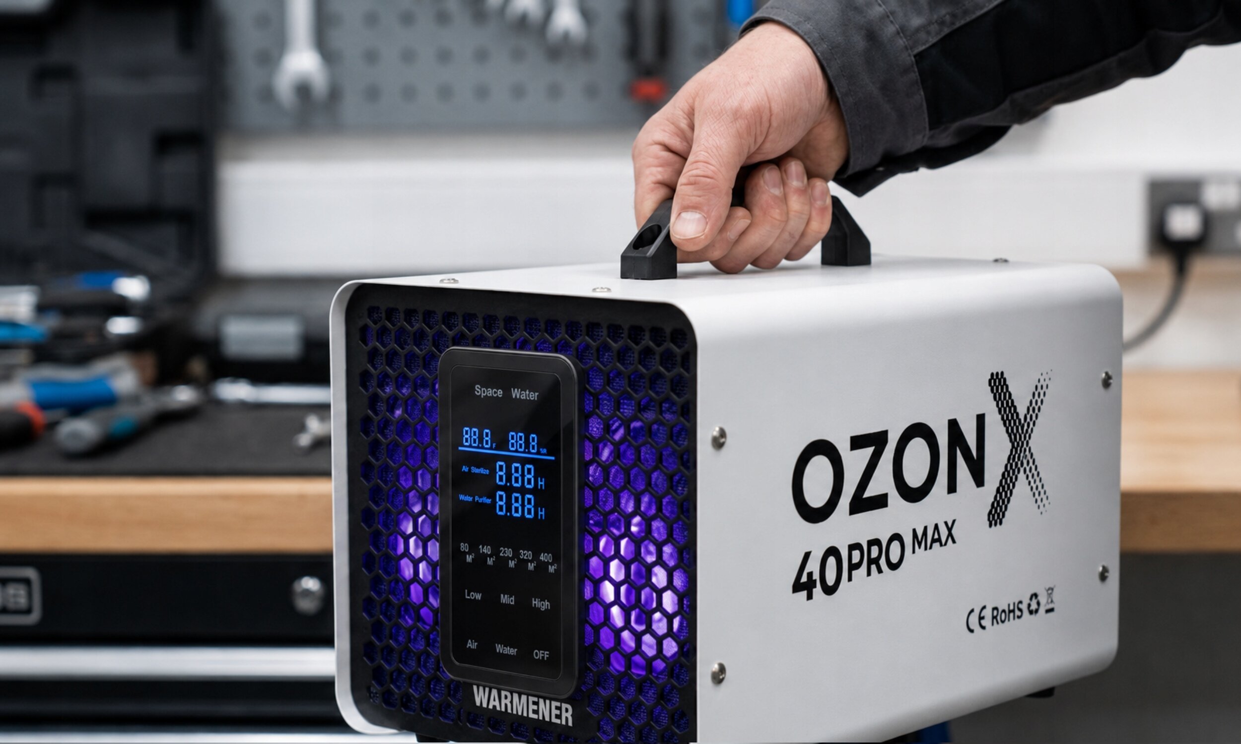 Osoba trzyma urządzenie oznaczone jako OZON X 40PRO MAX z wyświetlaczem pokazującym wartości 88.8 i napisem WARMENER. Urządzenie ma białą obudowę z czarnym panelem i niebieskim podświetleniem.