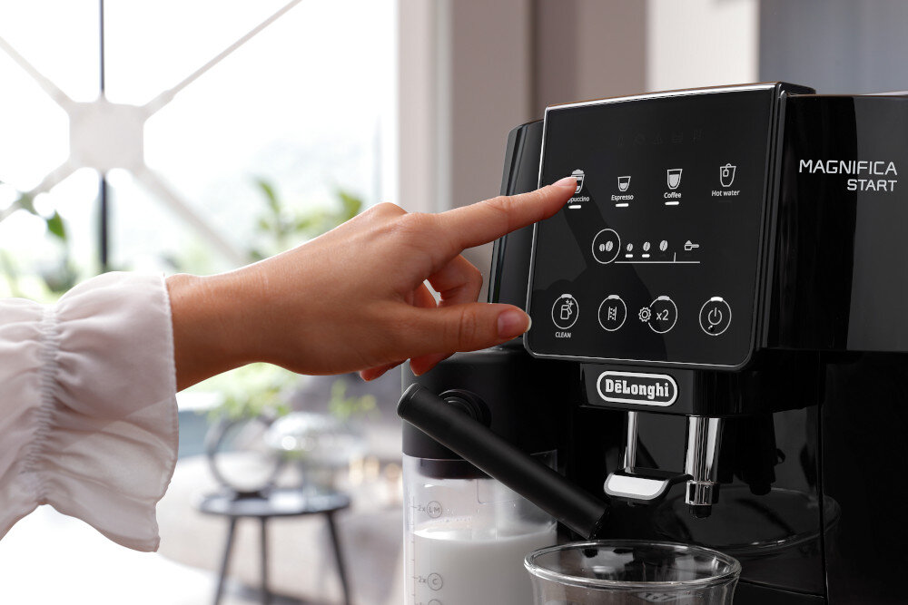 Osoba dotyka panelu sterowania ekspresu do kawy z widocznymi ikonami i napisem \'DeLonghi\'. Na panelu widoczne są przyciski do wyboru różnych rodzajów kawy oraz funkcji czyszczenia.