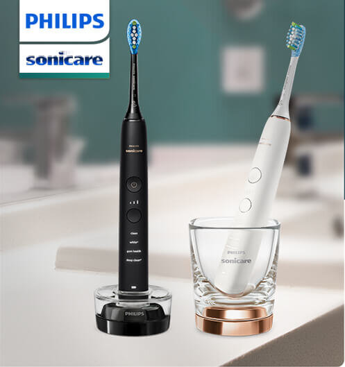 Na obrazie widoczne są dwie szczoteczki soniczne marki PHILIPS w kolorach czarnym i białym, umieszczone na podstawach ładujących. Obok znajduje się szklanka z funkcją ładowania, a w tle widoczne jest logo PHILIPS sonicare.