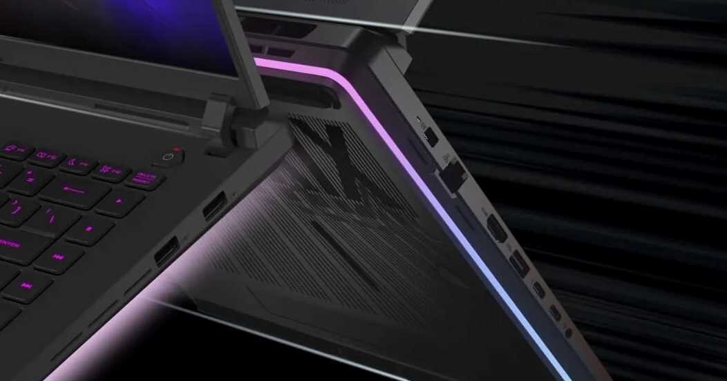 Zbliżenie na otwarty laptop z podświetlaną klawiaturą i kolorowym paskiem świetlnym na obudowie. Widoczne są porty USB oraz przycisk zasilania.