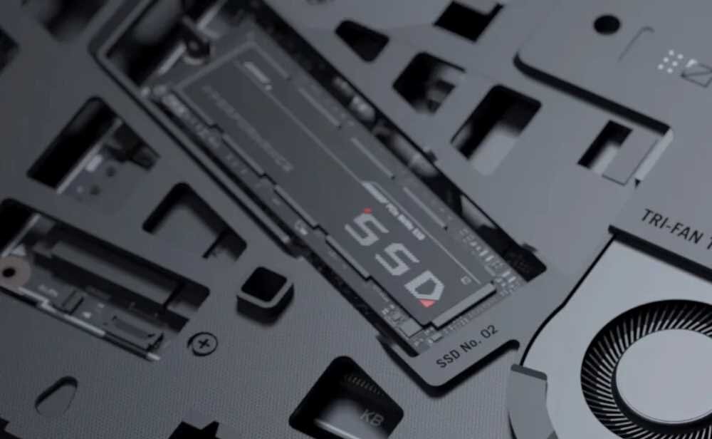 Zbliżenie na wnętrze laptopa z widocznym dyskiem SSD oznaczonym jako \'SSD No. 02\'. Obok znajduje się wentylator z napisem \'TRI-FAN\'.
