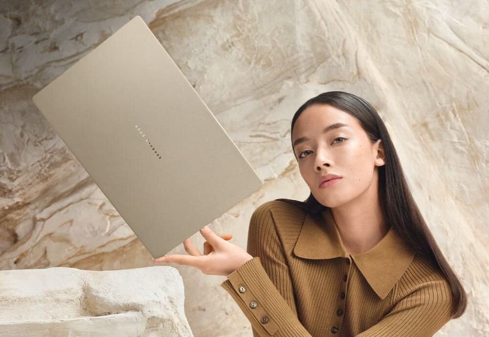 Osoba prezentuje laptop ASUS Zenbook A16 UX3607QA-SH039W z funkcją Copilot unosząc go dłonią na tle jasnych skał w otoczeniu - Copilot+ PC