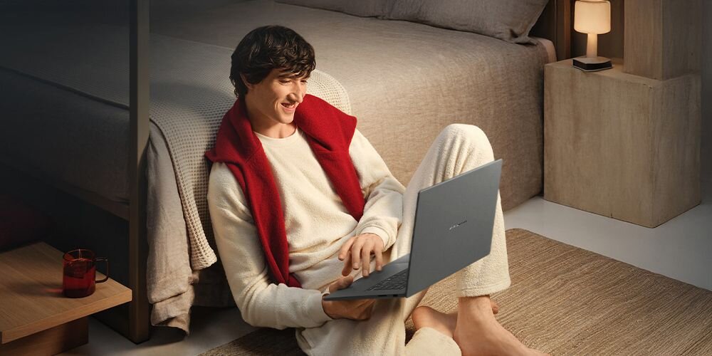 Laptop ASUS Zenbook A16 unosi się na tle nieba z chmurami, prezentując smukłą konstrukcję w nowoczesnym kontekście pracy mobilnej
