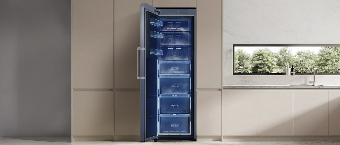 Zamrażarka z technologią All Around Cooling Zamrażarka szufladowa z otwartymi drzwiami, ukazująca kilka przezroczystych szuflad wewnątrz. Znajduje się w nowoczesnej kuchni z jasnymi szafkami i dużym oknem.