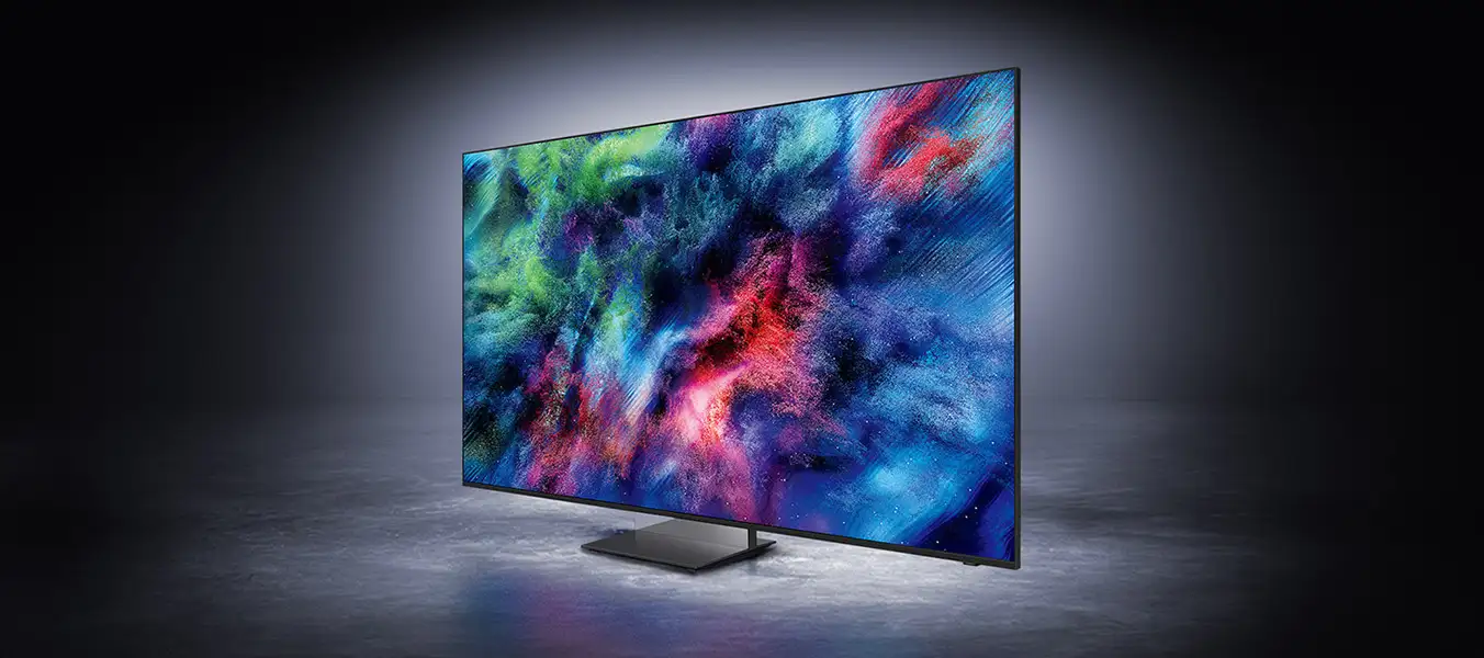 2026-micro-rgb-infinity-air-design-pc 1352x600 Telewizor z dużym ekranem wyświetlający kolorową, abstrakcyjną grafikę. Urządzenie stoi na ciemnej powierzchni w oświetlonym otoczeniu.