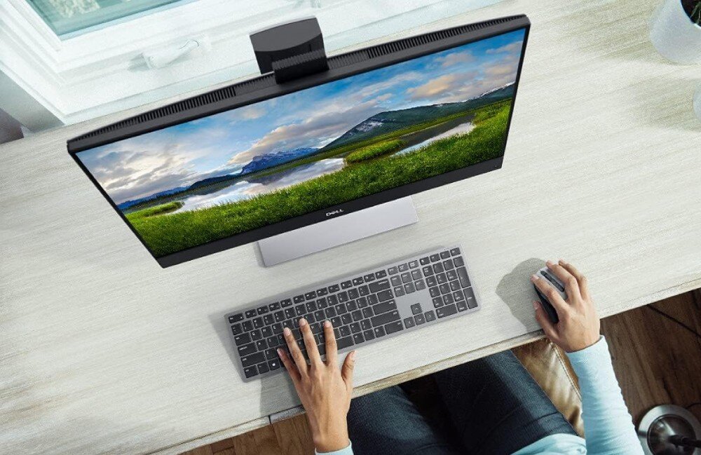 Na biurku znajduje się monitor z krajobrazem na ekranie, klawiatura i mysz. Na monitorze widoczne jest logo \'DELL\'.