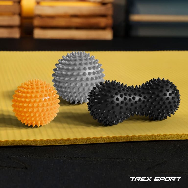 Na zdjęciu znajdują się trzy kolorowe piłeczki sensoryczne z wypustkami, umieszczone na żółtej macie. W prawym dolnym rogu widoczne jest logo \'TREX SPORT\'.