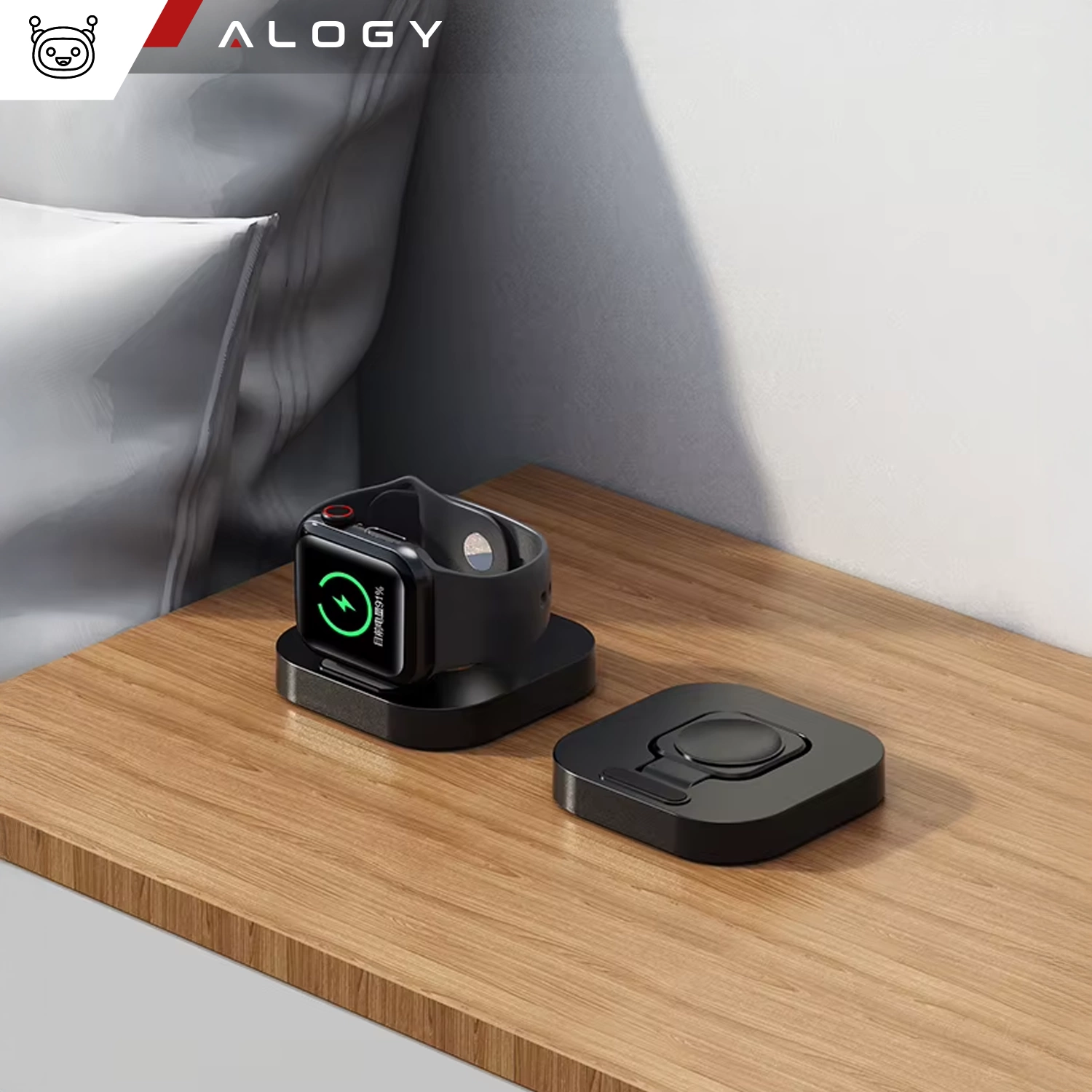 Na drewnianym blacie znajduje się czarna ładowarka magnetyczna z umieszczonym na niej zegarkiem Apple Watch, obok leży druga część ładowarki. W lewym górnym rogu widoczne jest logo \'ALOGY\'.