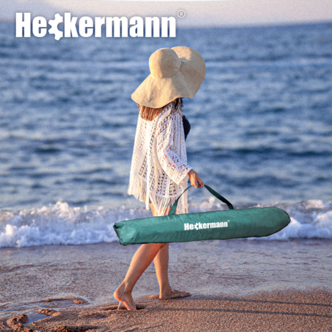 Osoba na plaży trzyma zielony pokrowiec z napisem \'Heckermann\', w tle widoczny jest ocean. W lewym górnym rogu znajduje się logo \'Heckermann\'.