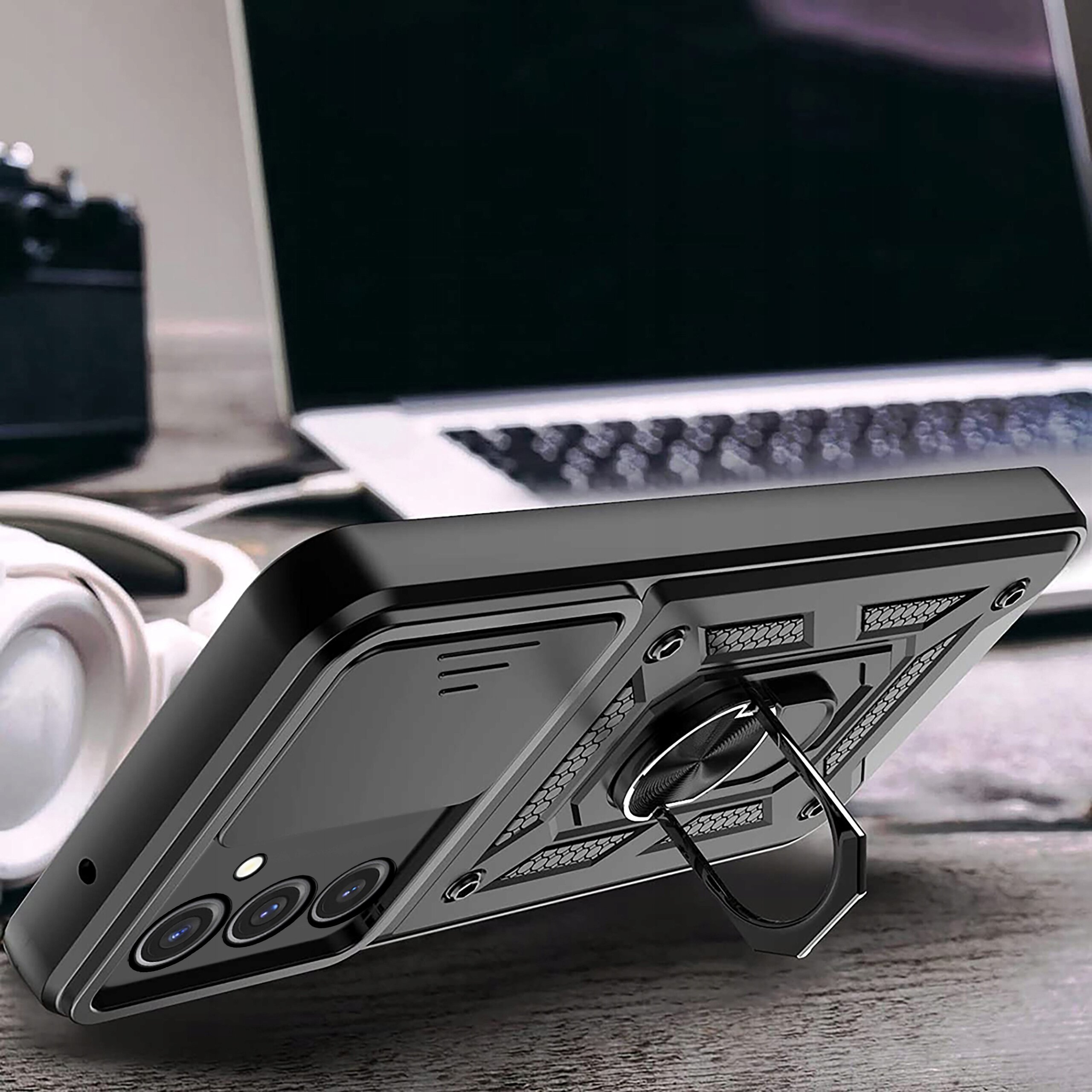 Etui do telefonu z pierścieniem na tylnej części, leżące na biurku obok słuchawek i otwartego laptopa.