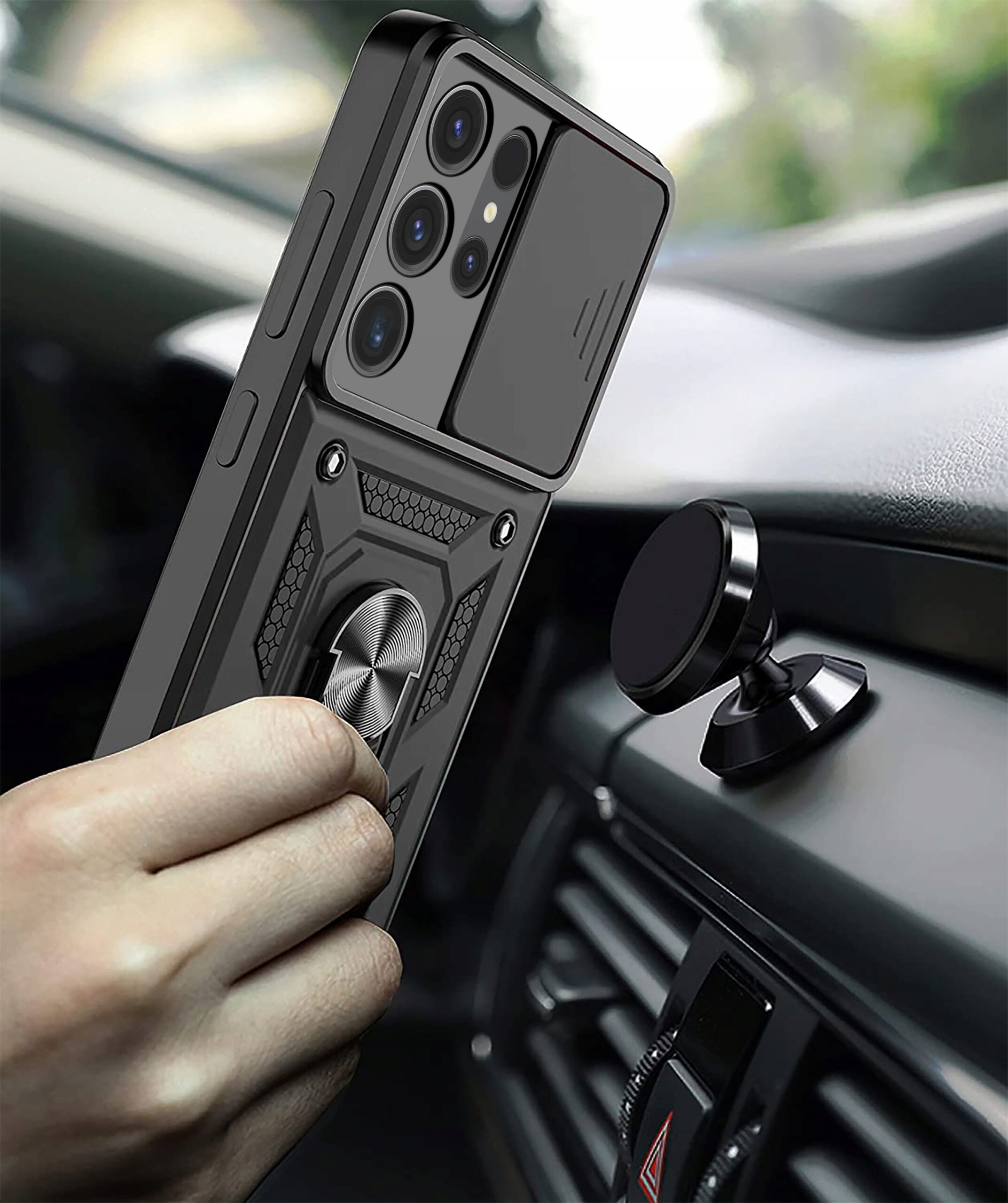 Osoba trzyma telefon w pancernym etui z pierścieniem, zbliżając go do magnetycznego uchwytu w samochodzie. Etui ma teksturowaną powierzchnię i widoczne są cztery obiektywy aparatu.