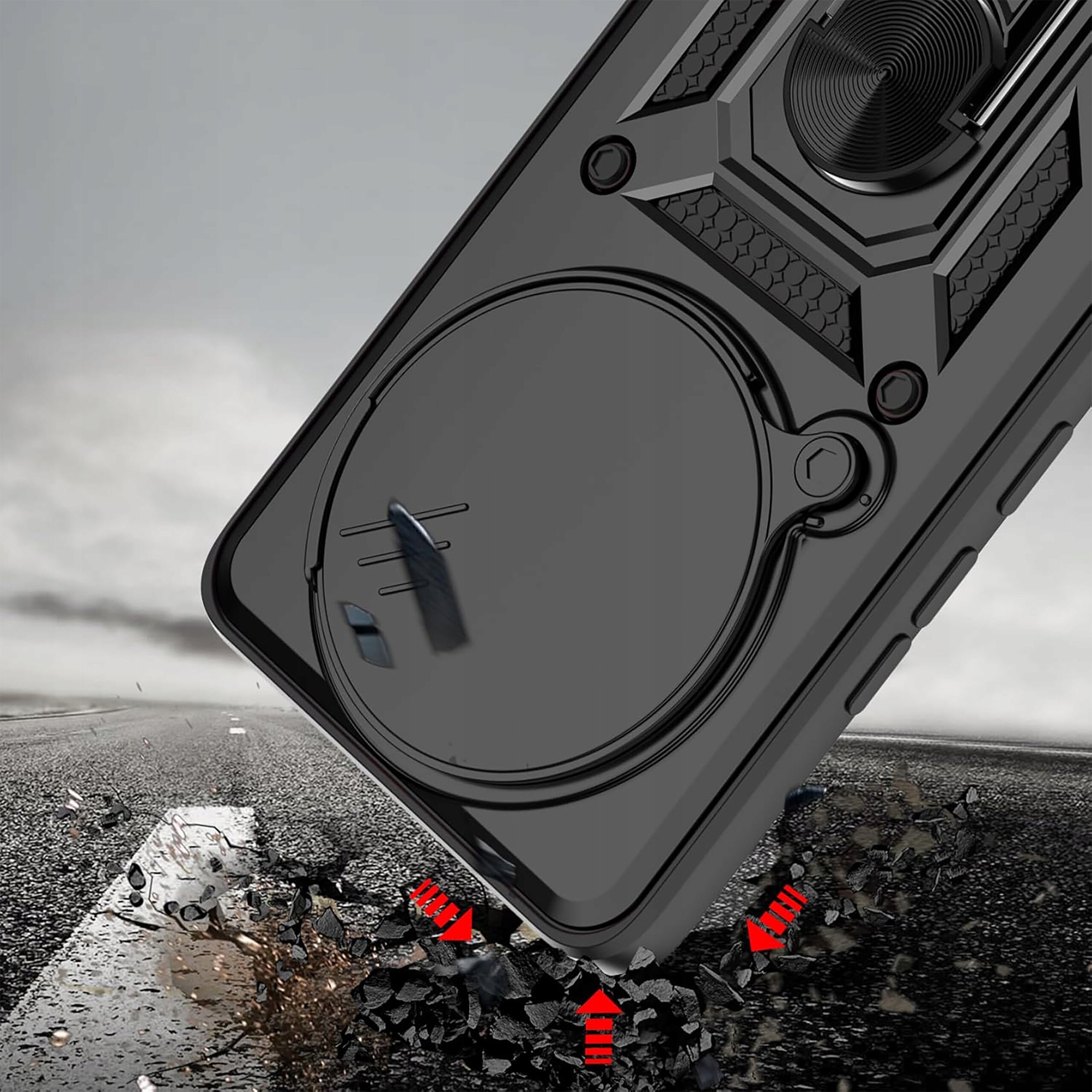 Zdjęcie przedstawia pancerne etui do telefonu z pierścieniem, leżące na drodze z pękającym asfaltem i czerwonymi strzałkami wskazującymi na wstrząsy. Tło jest rozmyte, a na etui widoczne są detale konstrukcyjne.
