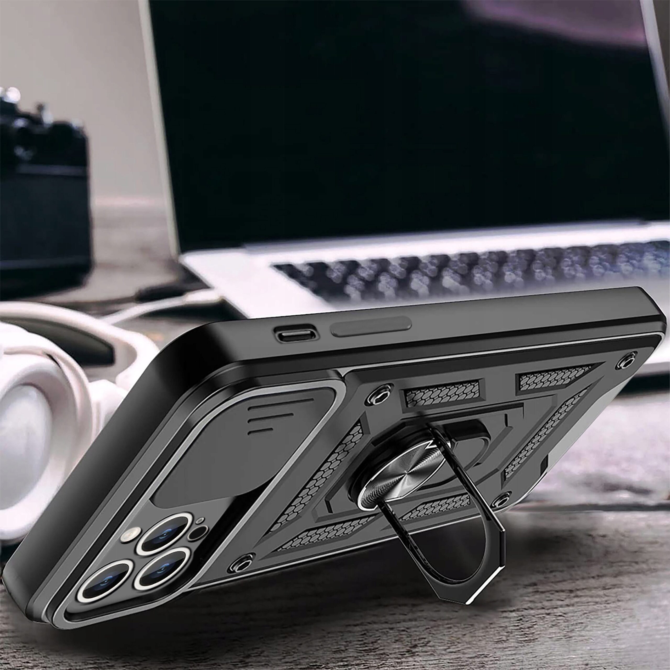 Etui do Samsung Galaxy S24 Fe w kolorze czarnym z wzmocnioną konstrukcją i pierścieniem do trzymania, leży na drewnianym stole obok słuchawek i laptopa.