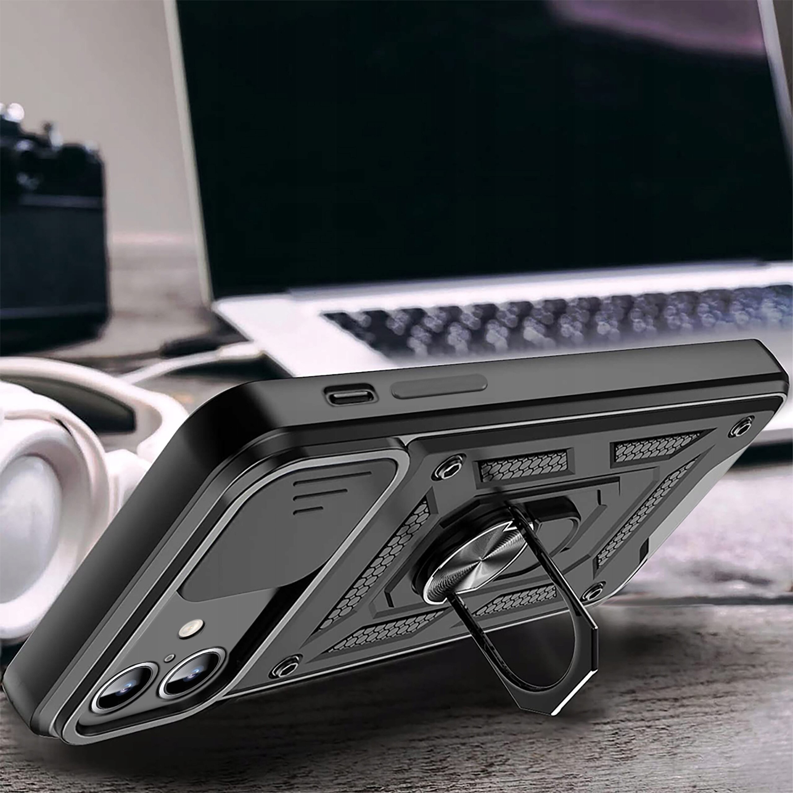 Etui do Samsung Galaxy S24 Fe w kolorze czarnym z wzmocnioną konstrukcją i pierścieniem do trzymania, leży na drewnianym stole obok słuchawek i laptopa.