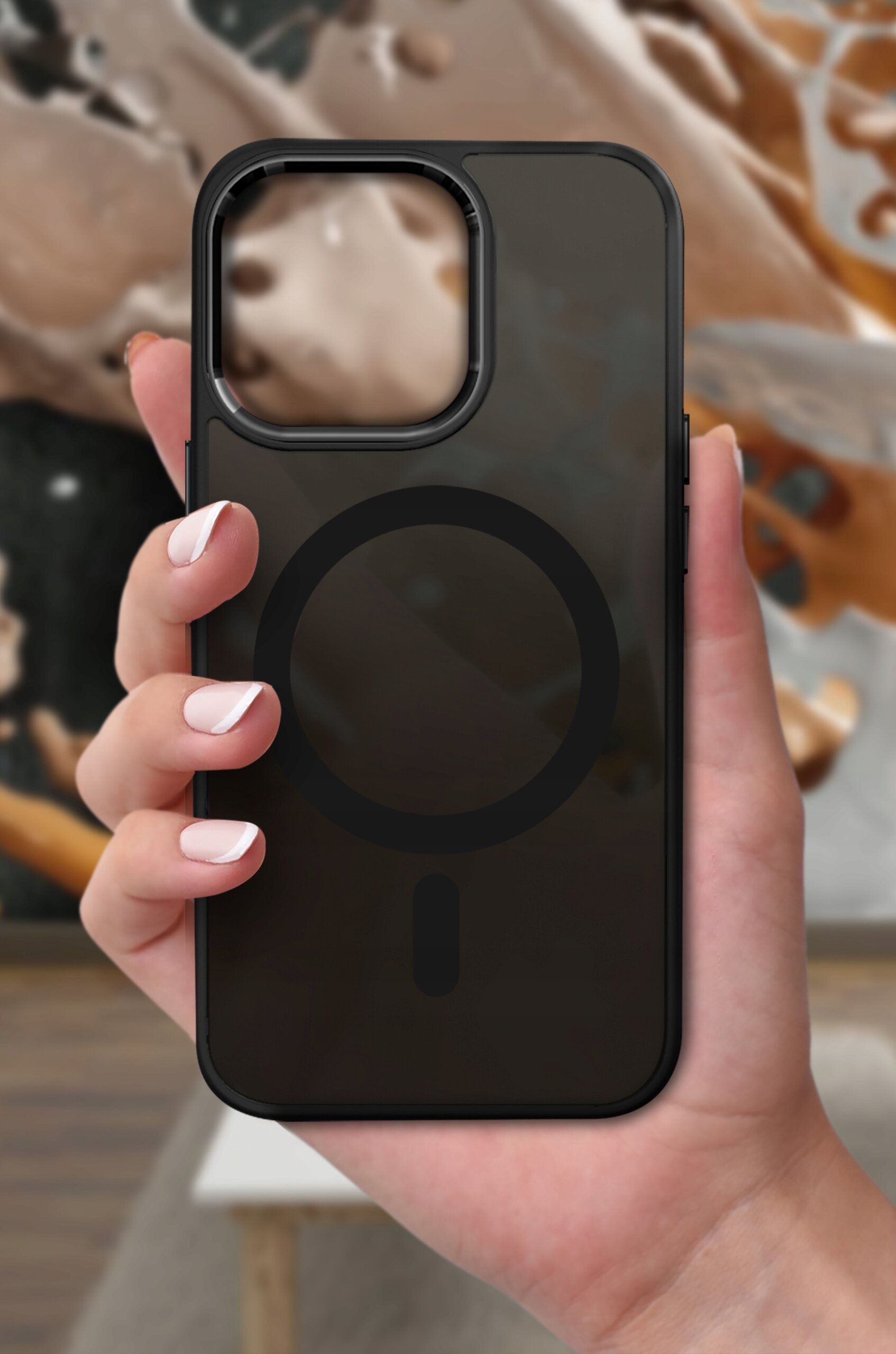 Osoba trzyma czarne, matowe etui do iPhone 15 Pro Max z widocznym okrągłym wzorem na środku. W tle znajduje się rozmyty obraz w odcieniach brązu i beżu.