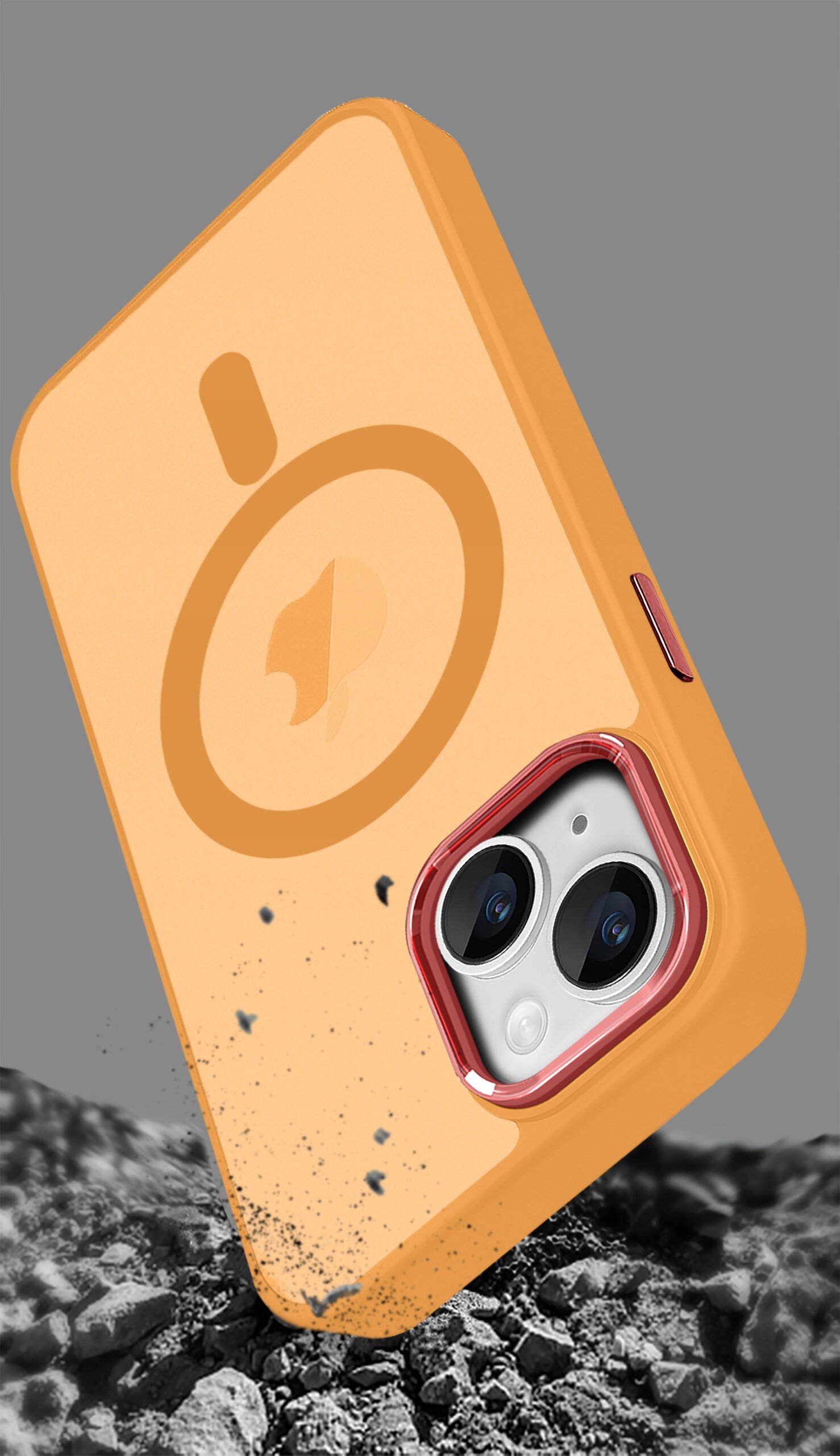 Pomarańczowe etui na telefon z widocznym logo w kształcie koła i strzałki, z wycięciem na aparat, leżące na tle szarego żwiru.