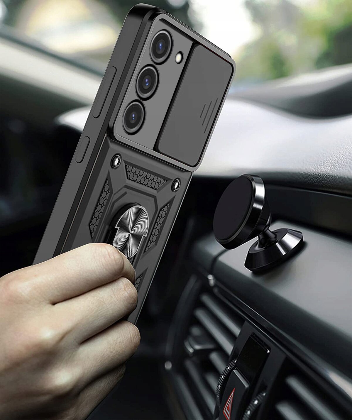 Osoba trzyma telefon w pancernym etui z pierścieniem, w pobliżu magnetycznego uchwytu samochodowego. Etui ma teksturowaną powierzchnię i trzy widoczne obiektywy aparatu.