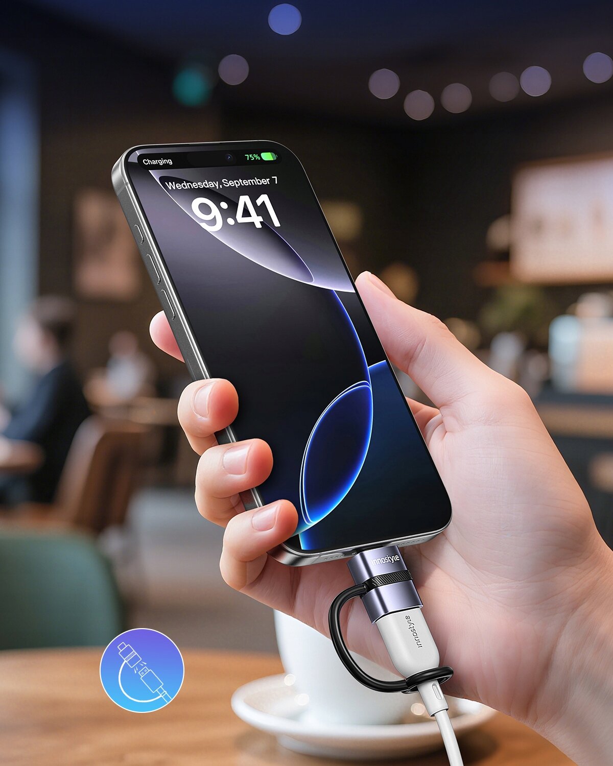 Osoba trzyma smartfon z wyświetlaczem pokazującym godzinę 9:41 i datę Wednesday, September 7, podłączony do adaptera USB-C z napisem \'Innostyle\'. W tle widoczna jest rozmyta kawiarnia.