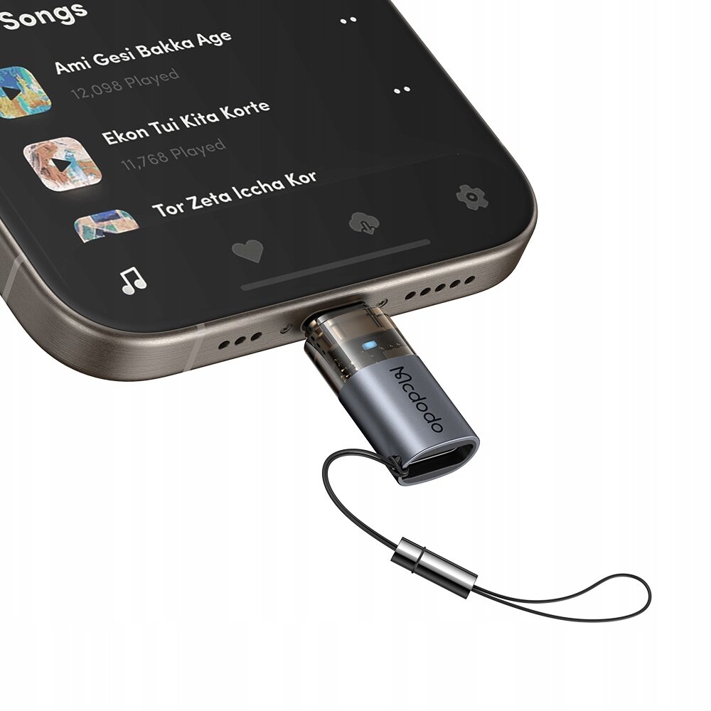 Adapter Mcdodo USB-C do Lightning podłączony do smartfona, z widocznym napisem \'Mcdodo\' na obudowie adaptera. Na ekranie telefonu wyświetlona jest lista utworów z tytułami: \'Ami Gesi Bakka Age\', \'Ekon Tui Kita Korte\', \'Tor Zeta Iccha Kor\'.