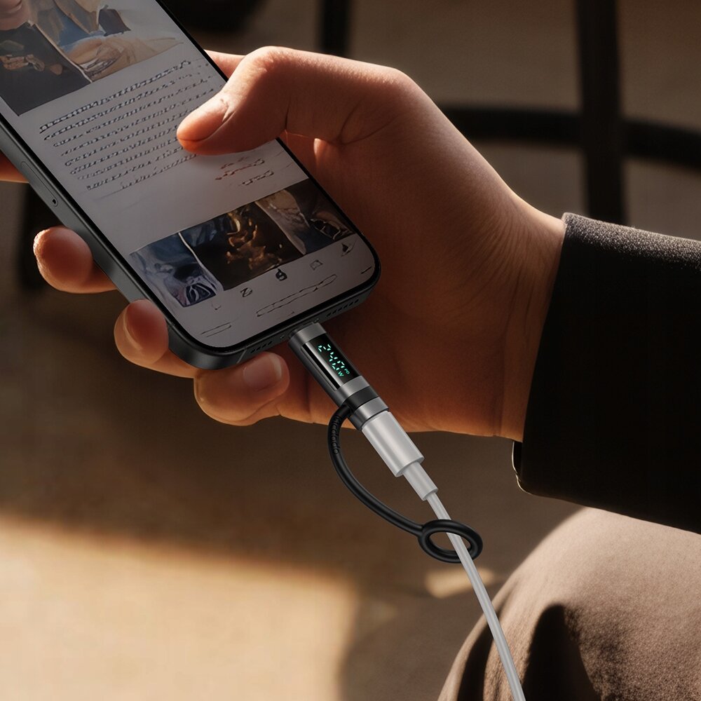 Osoba trzyma smartfon z podłączonym adapterem USB-C do Lightning, na którym widoczny jest wyświetlacz z zielonymi cyframi. Na ekranie telefonu widoczne są zdjęcia i tekst, jednak nieczytelne.