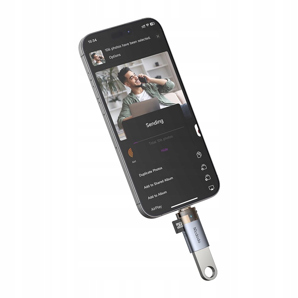 Zdjęcie przedstawia smartfon z ekranem pokazującym aplikację do przesyłania zdjęć, do którego podłączony jest adapter Mcdodo z czytnikiem kart TF. Na ekranie widoczny jest napis \'106 photos have been selected\' oraz \'Sending\'.