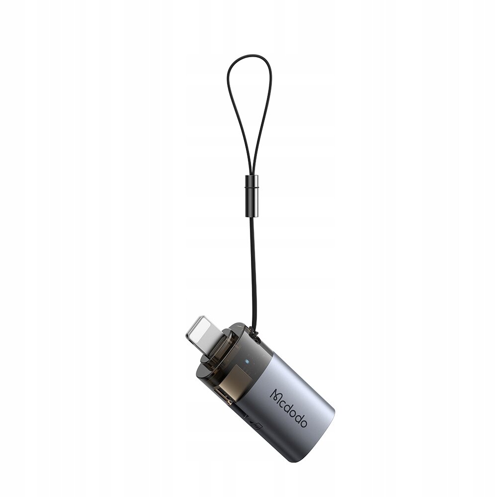 Na obrazie widoczny jest adapter w kolorze szarym z logo \'Mcdodo\', posiadający złącze USB-A i Lightning oraz czarną smyczkę. Adapter ma kompaktowy, cylindryczny kształt.