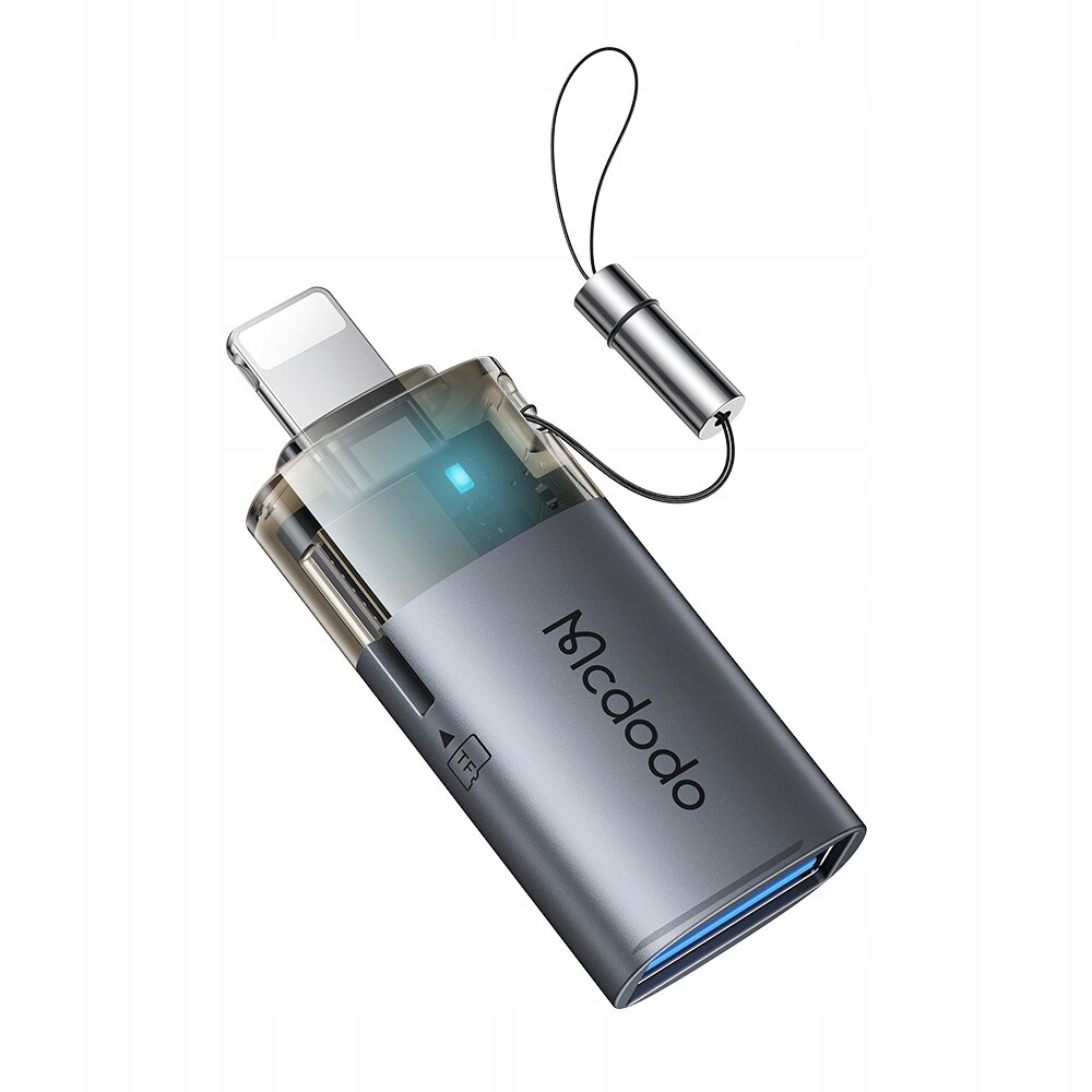 Na obrazie widoczny jest adapter USB-A do Lightning z czytnikiem kart TF, oznaczony logo \'Mcdodo\'. Adapter ma metaliczną obudowę i przezroczystą część z widocznym złączem Lightning oraz niebieskim wskaźnikiem LED.