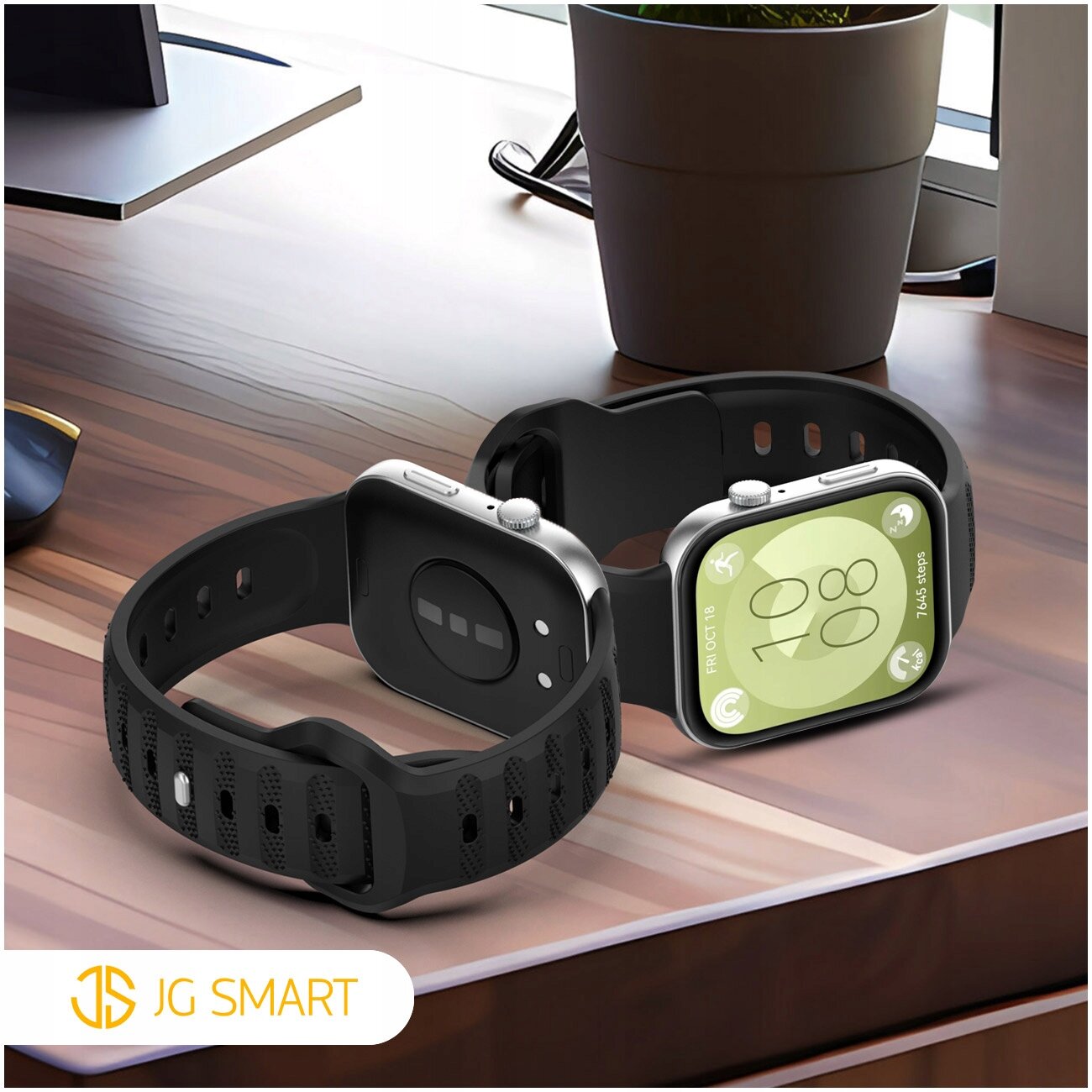 Na drewnianym biurku znajdują się dwa smartwatche z czarnymi silikonowymi paskami. W lewym dolnym rogu widoczne jest logo \'JG SMART\'.